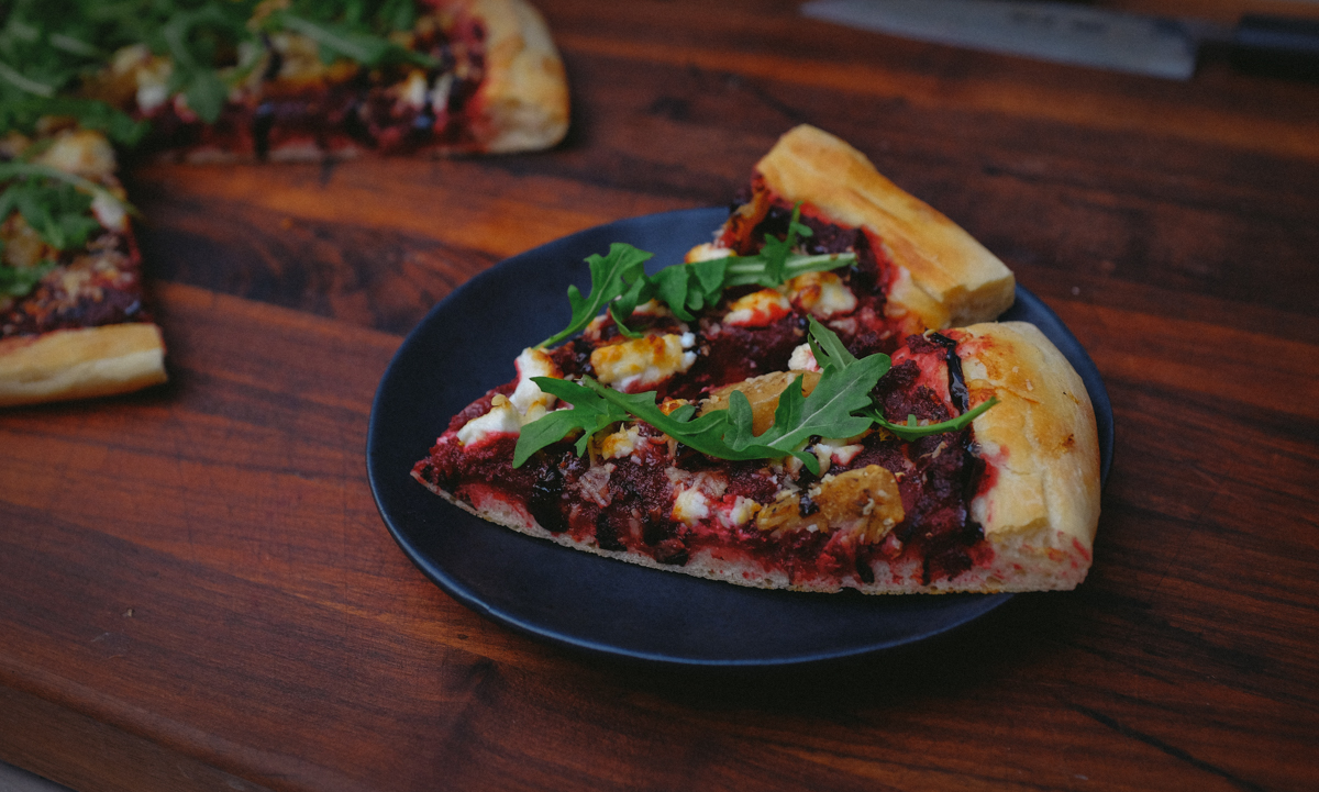 Pizza with roasted beet and garlic sauce topped with goat cheese, parmesean, and arugula